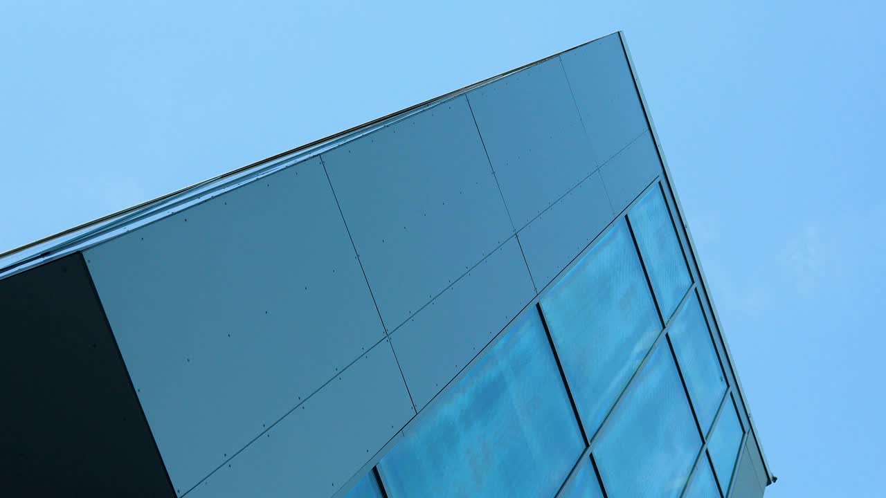 现代建筑角落，光滑的面板和反光的蓝色玻璃映衬着晴朗的天空。视频素材