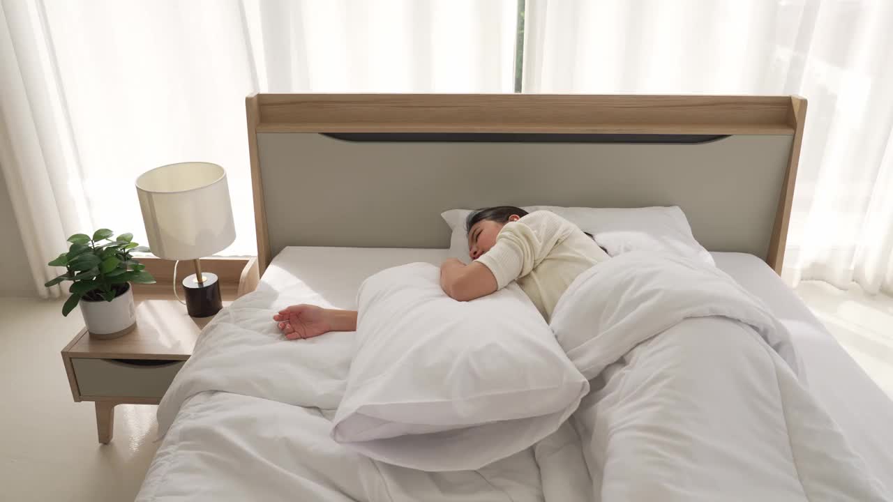 懒惰的亚洲女性不愿起床工作。躺下的时候用枕头盖住耳朵。生活方式概念，广角镜头。视频下载
