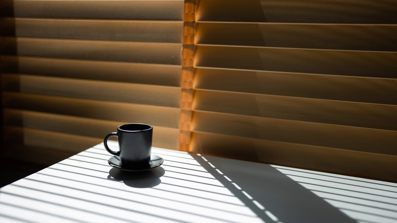 清晨日出时，明亮的阳光透过百叶窗照射进来，黑影出现在咖啡馆的黑色咖啡杯和咖啡桌上。视频下载
