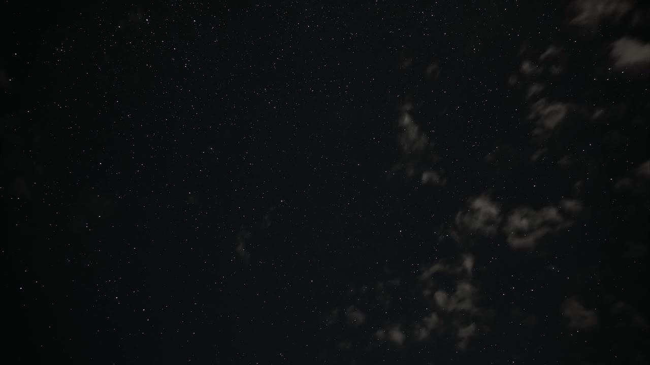 在漆黑的夜空中，星星和白云的延时运动作为背景视频下载