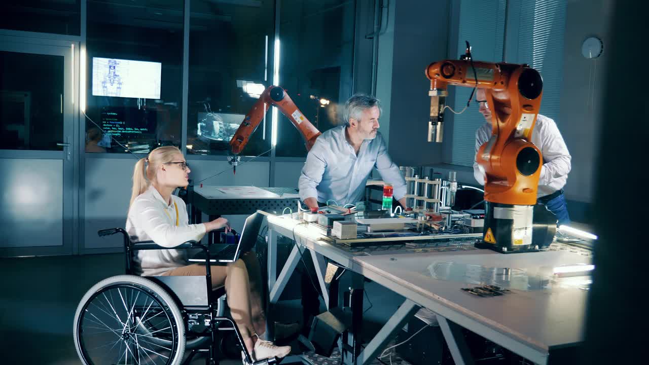 坐在轮椅上的工程师在一家现代化工厂与团队一起工作。视频下载