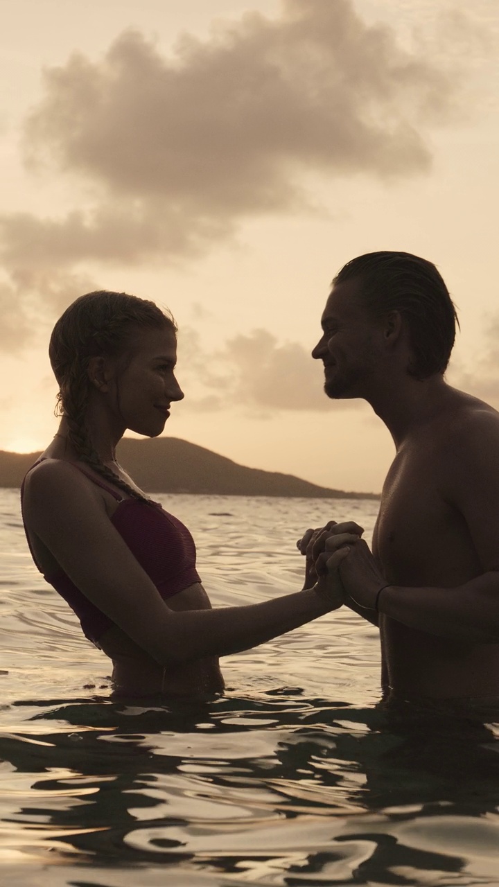 浪漫的情侣手牵着手，在日落的海洋亲吻-垂直视频/詹姆斯比岛，多巴哥群岛，圣文森特和格林纳丁斯视频下载