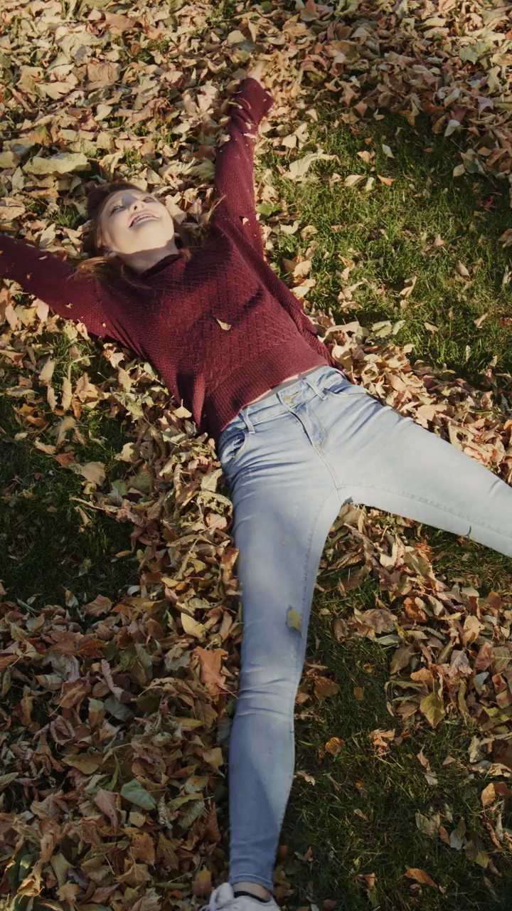高角度的女孩躺在秋叶制作天使-垂直视频/雪松山，犹他州，美国视频下载