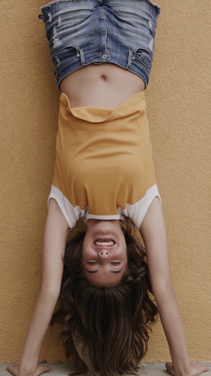 微笑的女孩对墙倒立的慢动作肖像-垂直录像/普罗沃，犹他州，美国视频下载