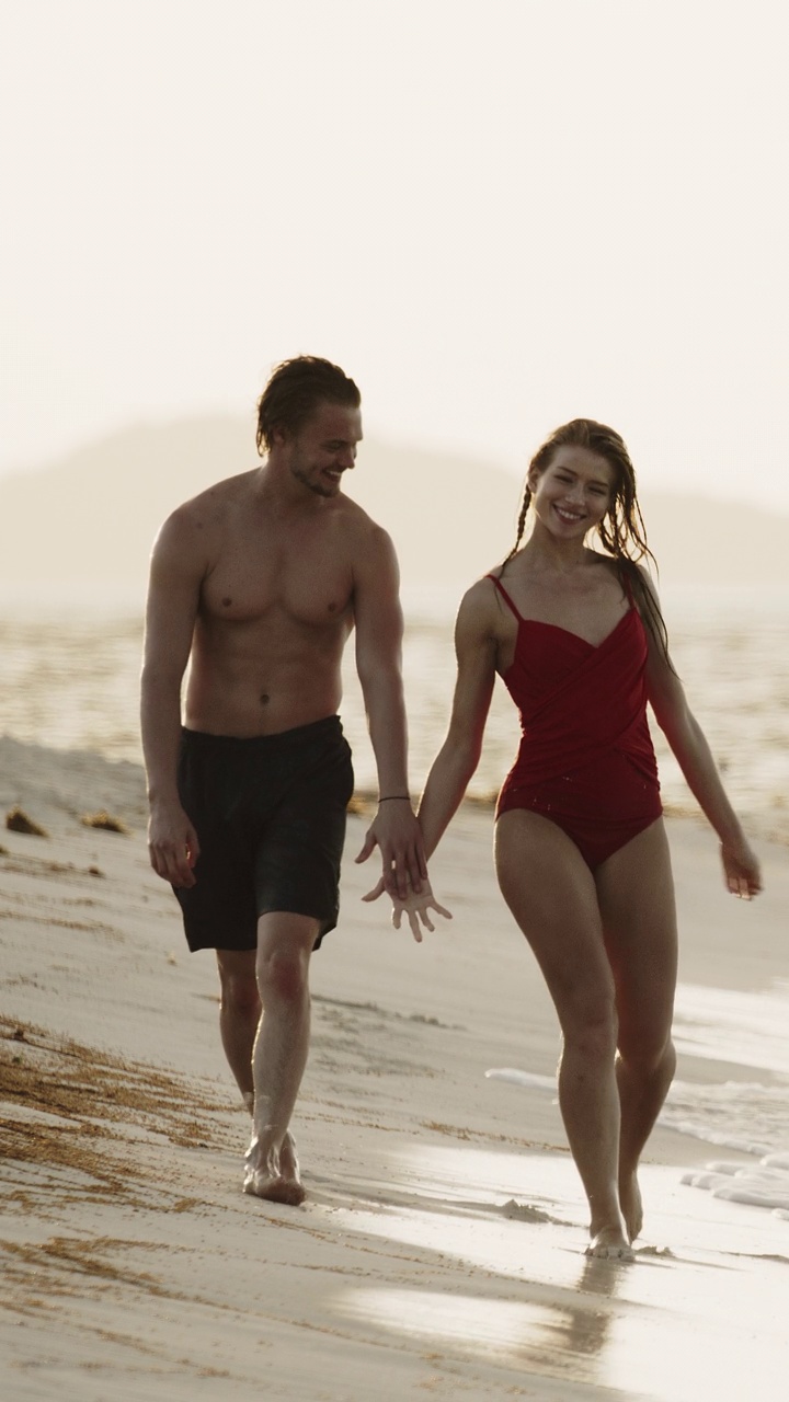 浪漫的情侣手牵着手走在沙滩上亲吻的慢动作-垂直视频/小塔巴克，多巴哥群岛，圣文森特和格林纳丁斯视频下载