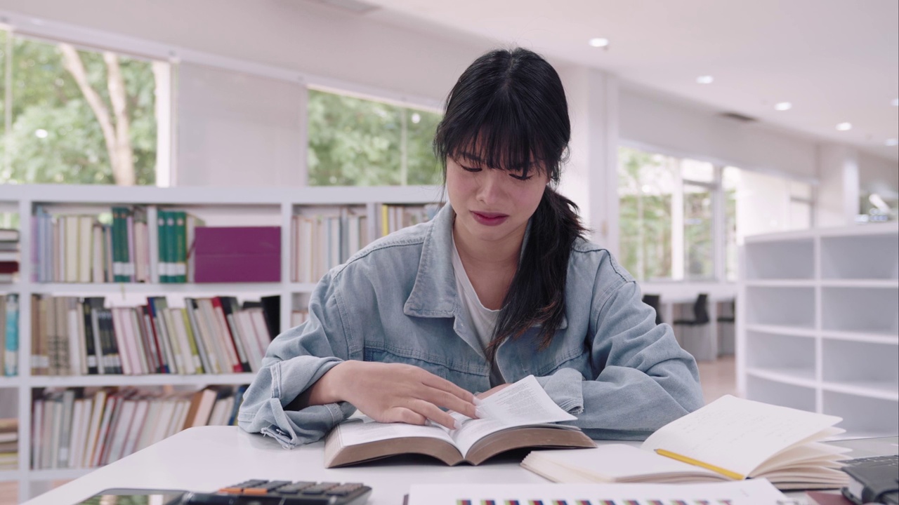 年轻的亚洲女大学生们在大学图书馆里阅读学习资料，研究课程，因为理解课程的困难而感到沮丧。视频下载