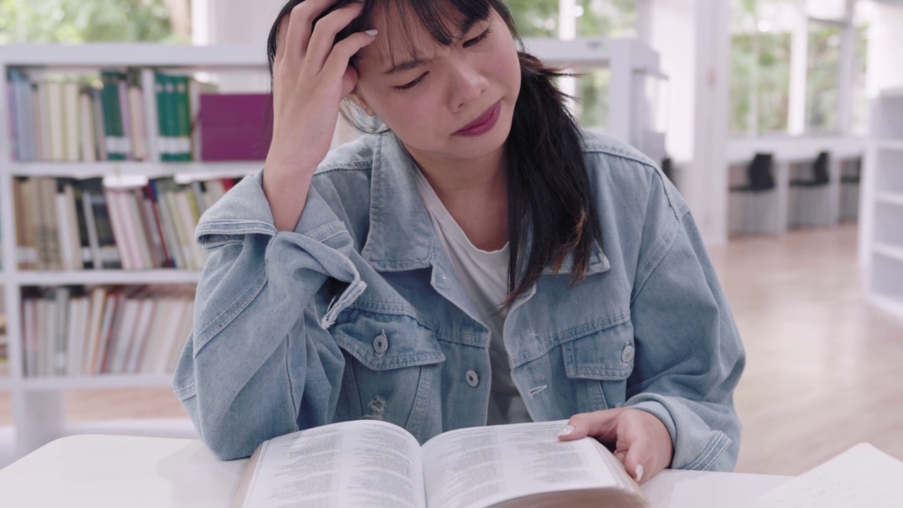 年轻的亚洲女大学生们在大学图书馆里阅读学习资料，研究课程，因为理解课程的困难而感到沮丧。视频下载