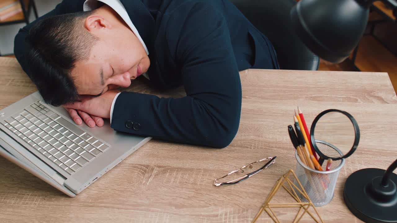 无聊困倦的商人工人靠在笔记本电脑上工作，趴在办公桌旁睡着了视频下载