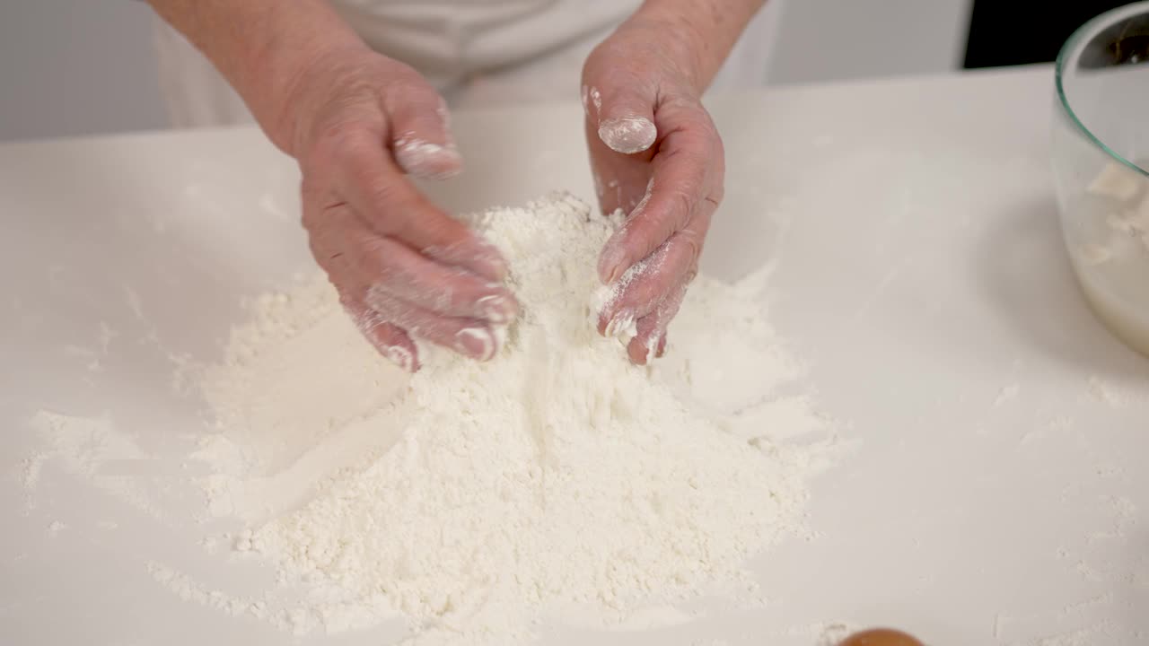 老妇人在厨房的桌子上用手收集面粉。家庭烹饪的概念视频下载