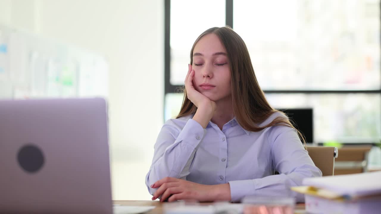 疲倦的年轻女实习生闭着眼睛坐在工作场所。视频下载