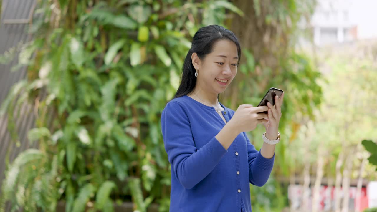 微笑的年轻亚洲女子在城市里使用智能手机视频素材