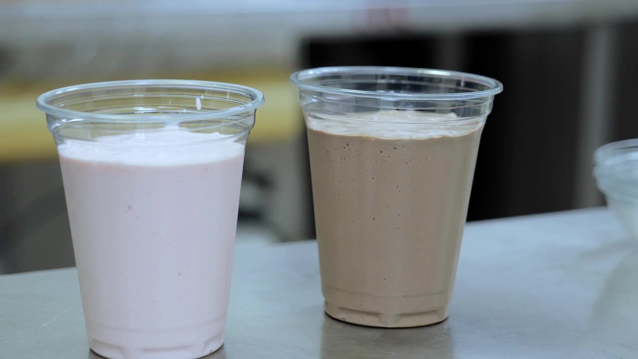奶昔美味的甜点饮料。巧克力奶昔倒入玻璃杯，草莓奶昔倒入冰淇淋和牛奶，草莓奶昔倒入塑料杯。视频素材