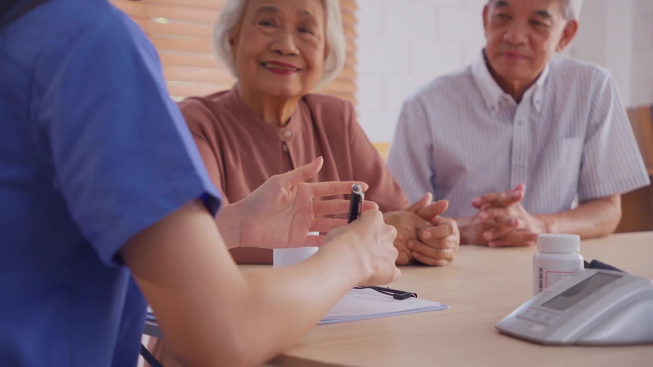 亚洲护理护士在家检查老年女病人和丈夫。有吸引力的年轻专家职业女孩支持给予建议和咨询老年夫妇在客厅里的房子。视频素材