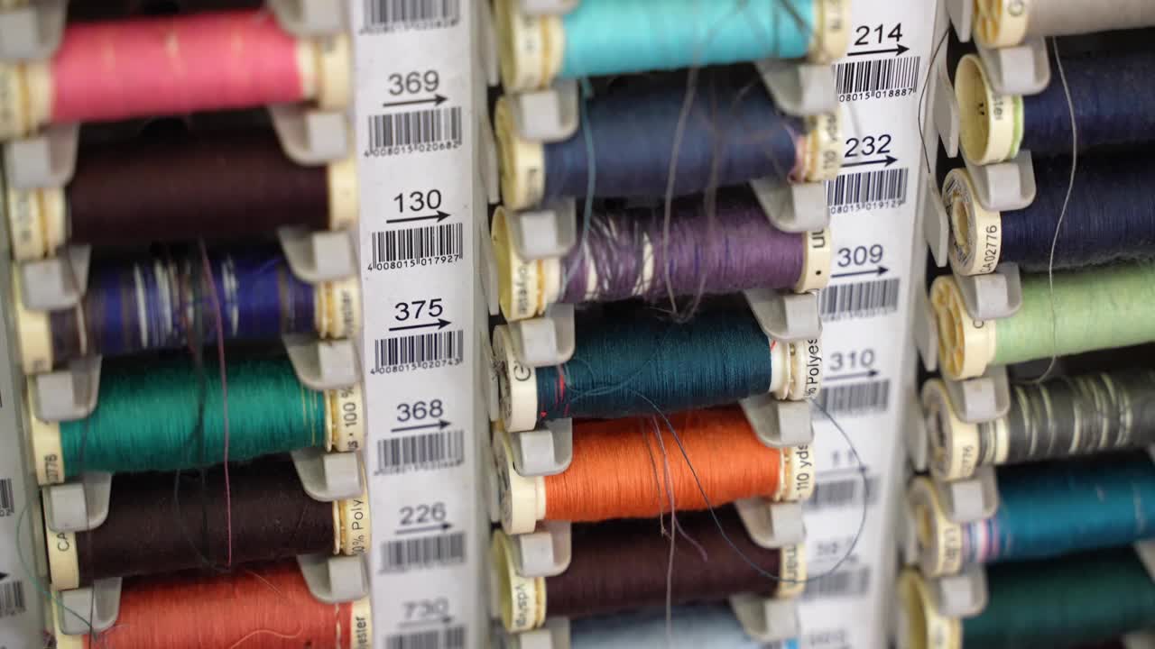 专业裁缝工坊的彩色棉线线轴的倾斜镜头，广泛收集的织物线卷，用于刺绣或工作室的衣服修补。裁缝视频素材
