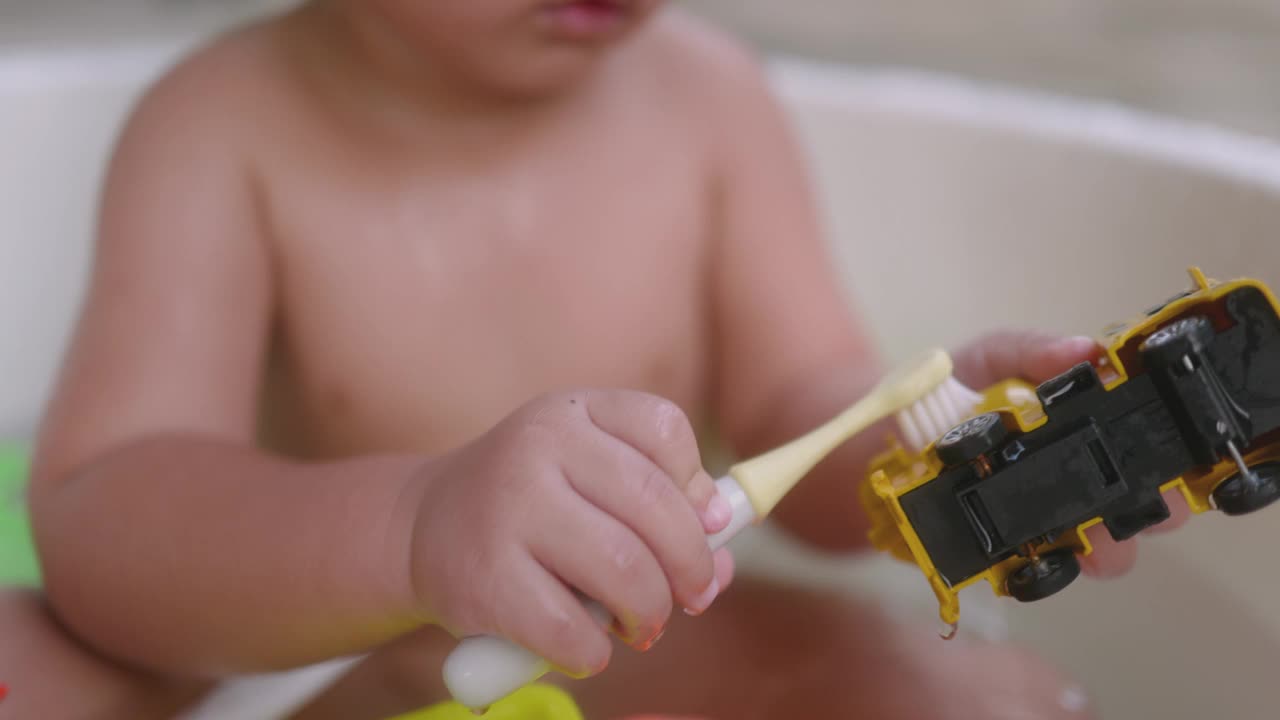 一个亚洲男孩正在家里和他妈妈一起玩玩具，在盆里洗澡。用牙刷刷洗玩具。视频下载