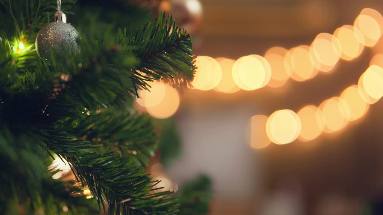 在宁静的冬夜，在家中的节日灯光背景下，妇女用装饰物装饰圣诞树的特写手，圣诞节和新年的概念。视频下载
