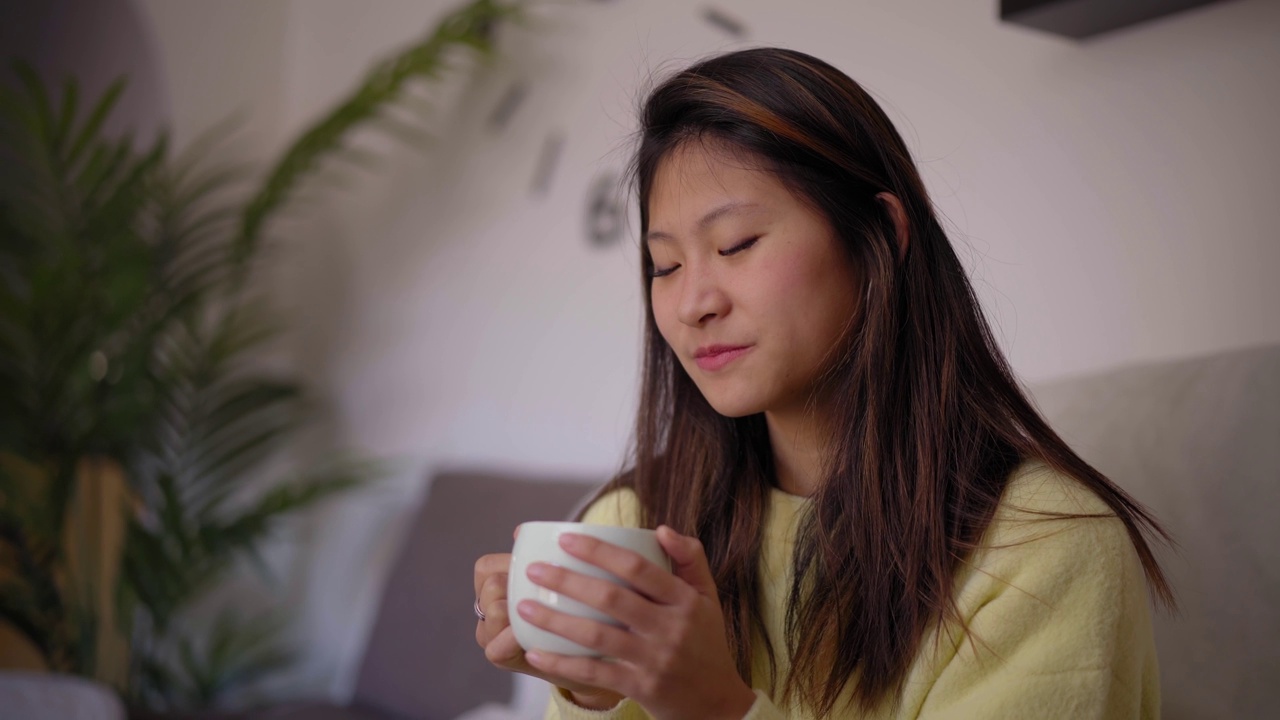 中国女孩在家里享受早晨在客厅喝热咖啡或茶。视频下载
