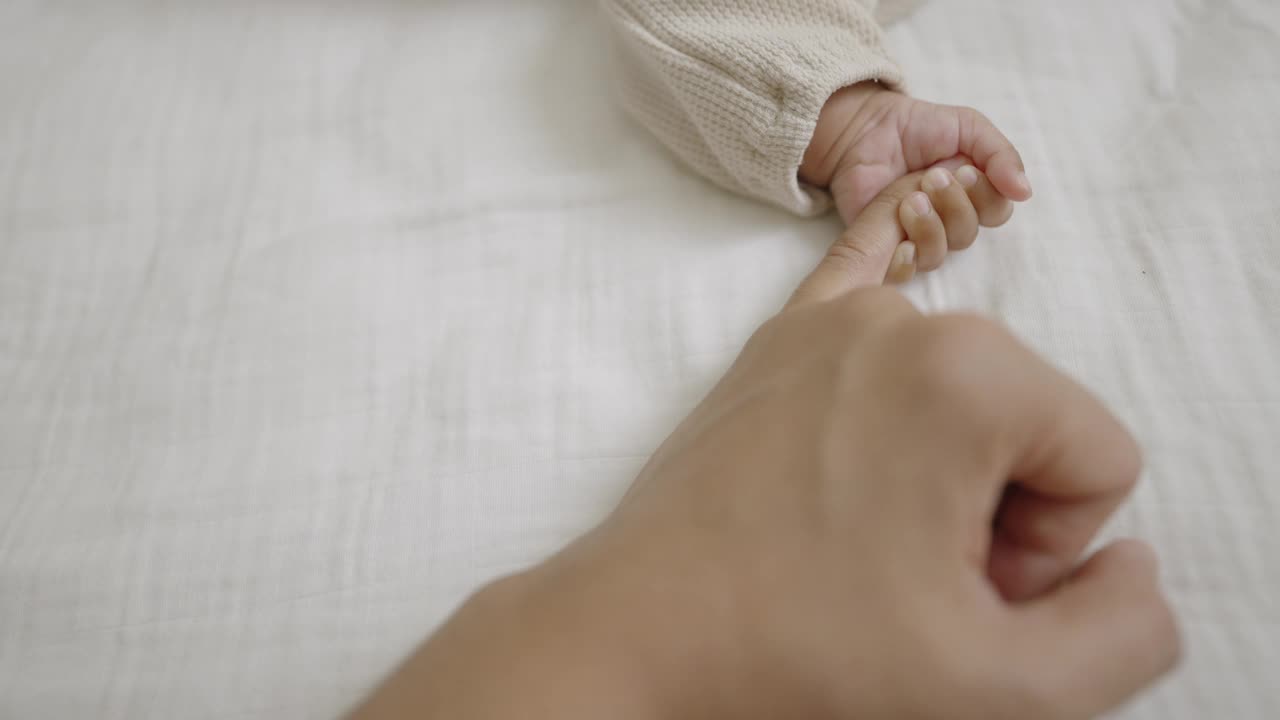 慢镜头:一个小男孩在床上睡觉时紧紧抓着妈妈的手指。视频下载