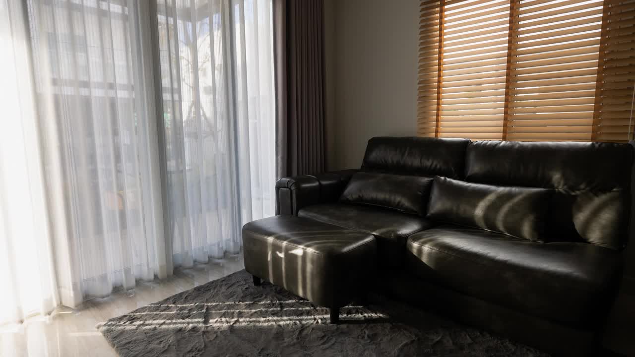 在安静的客厅里，明亮的阳光透过玻璃门和白色的窗帘照在黑色的沙发上。视频下载