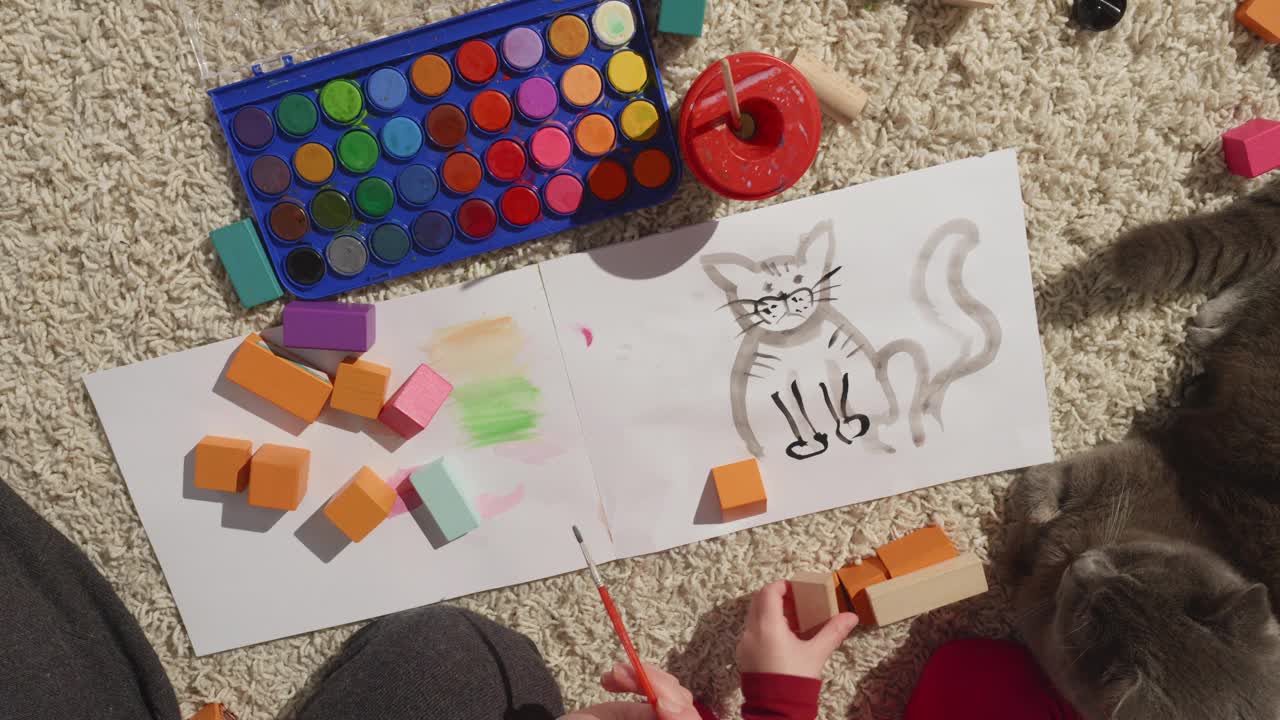 俯视图，妈妈的手画家庭宠物肖像与孩子和猫躺在附近视频下载