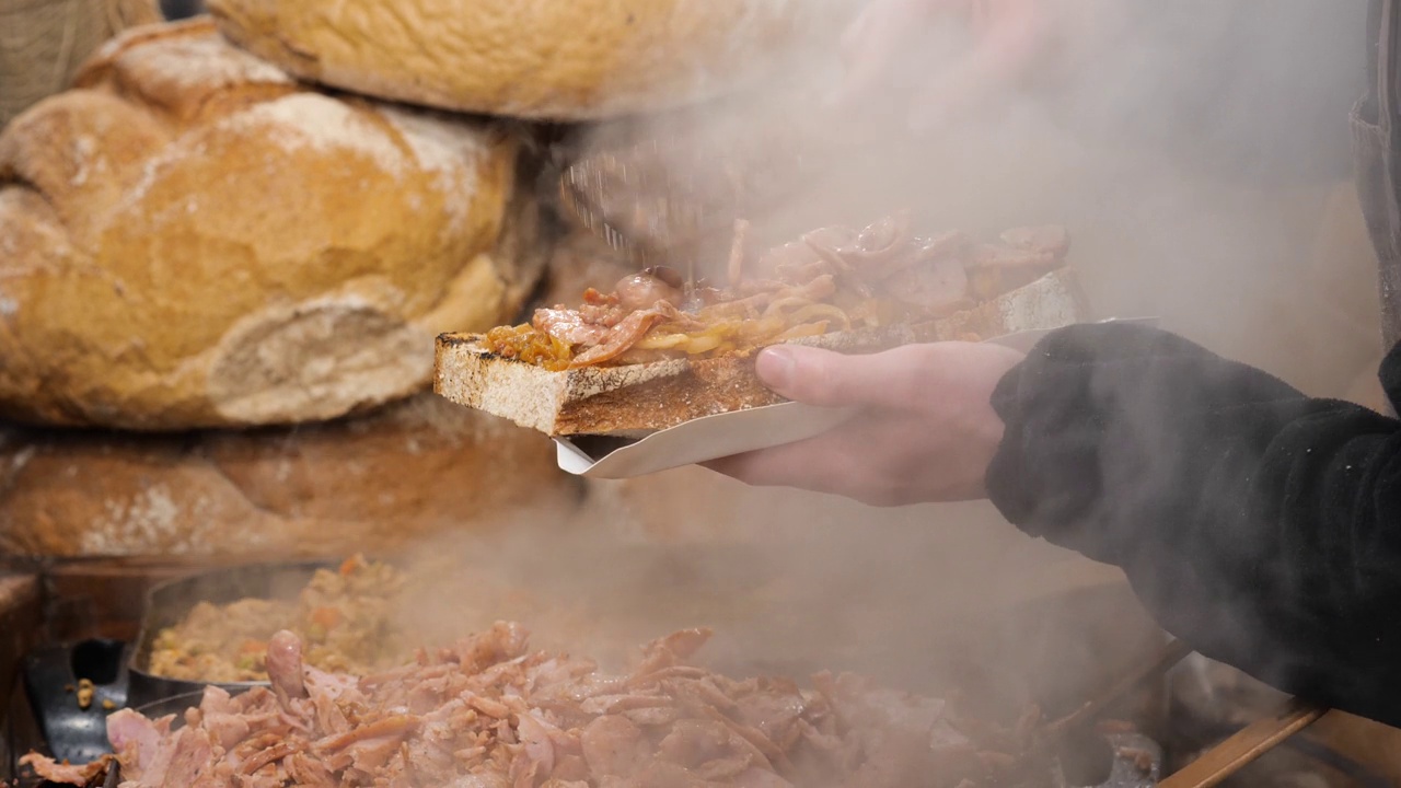 一名男子将烤好的洋葱和肉铺在一大片面包上，传统的波兰当地街头美食节，市场摊位特写，细节，食物准备。制作、准备传统的食物理念视频素材