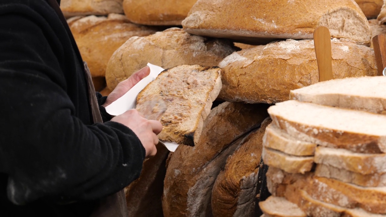 一名男子在一片大面包上涂猪油，波兰传统美食节市场摊位，买卖当地食品，特写，细节。有机健康食品企业，人，生活方式视频下载
