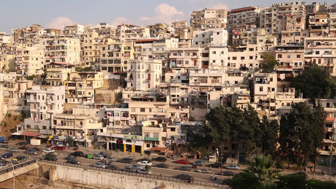 在黎巴嫩北部的的黎波里，沿着山坡上高耸的中东房屋行驶的道路视频下载