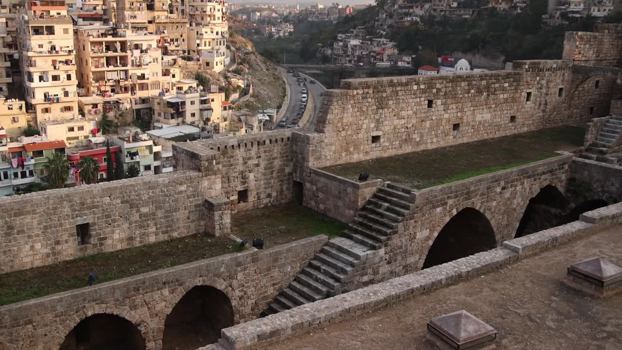 在黎巴嫩北部的黎波里，一个村庄坐落在丘陵和山谷中，通向一座古老的石头城堡废墟之上的山脉视频下载