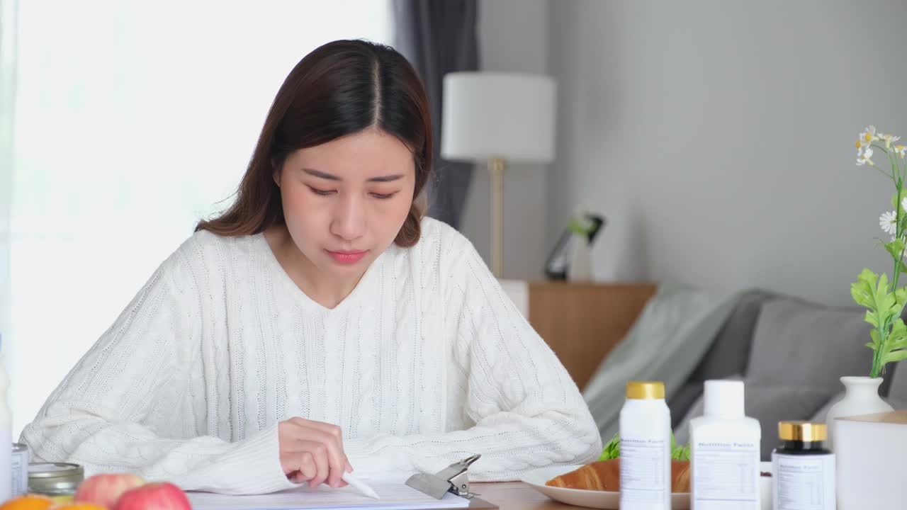 年轻的亚洲女性营养师阅读食品包装上的营养成分标签，并在纸上写数据，为客户提供健康饮食的建议视频下载