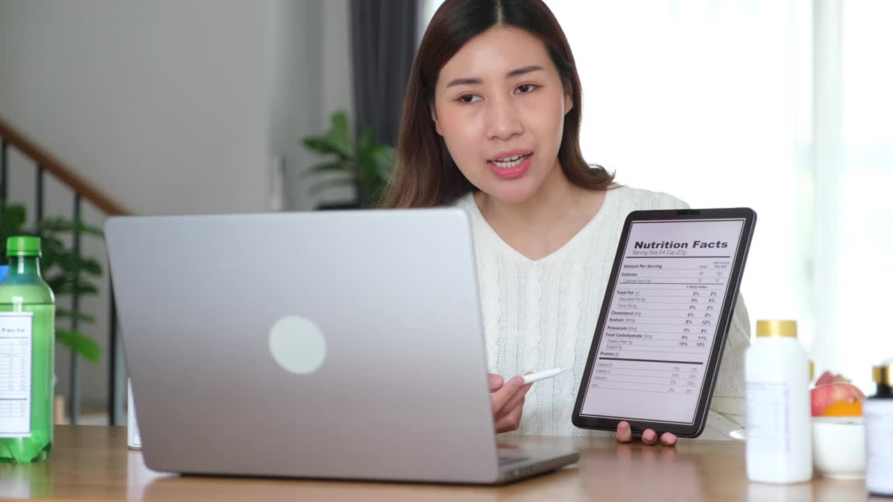 年轻的亚洲女性营养师通过笔记本电脑向客户展示营养事实，提供健康食品建议，制作视频博客，直播流媒体视频下载