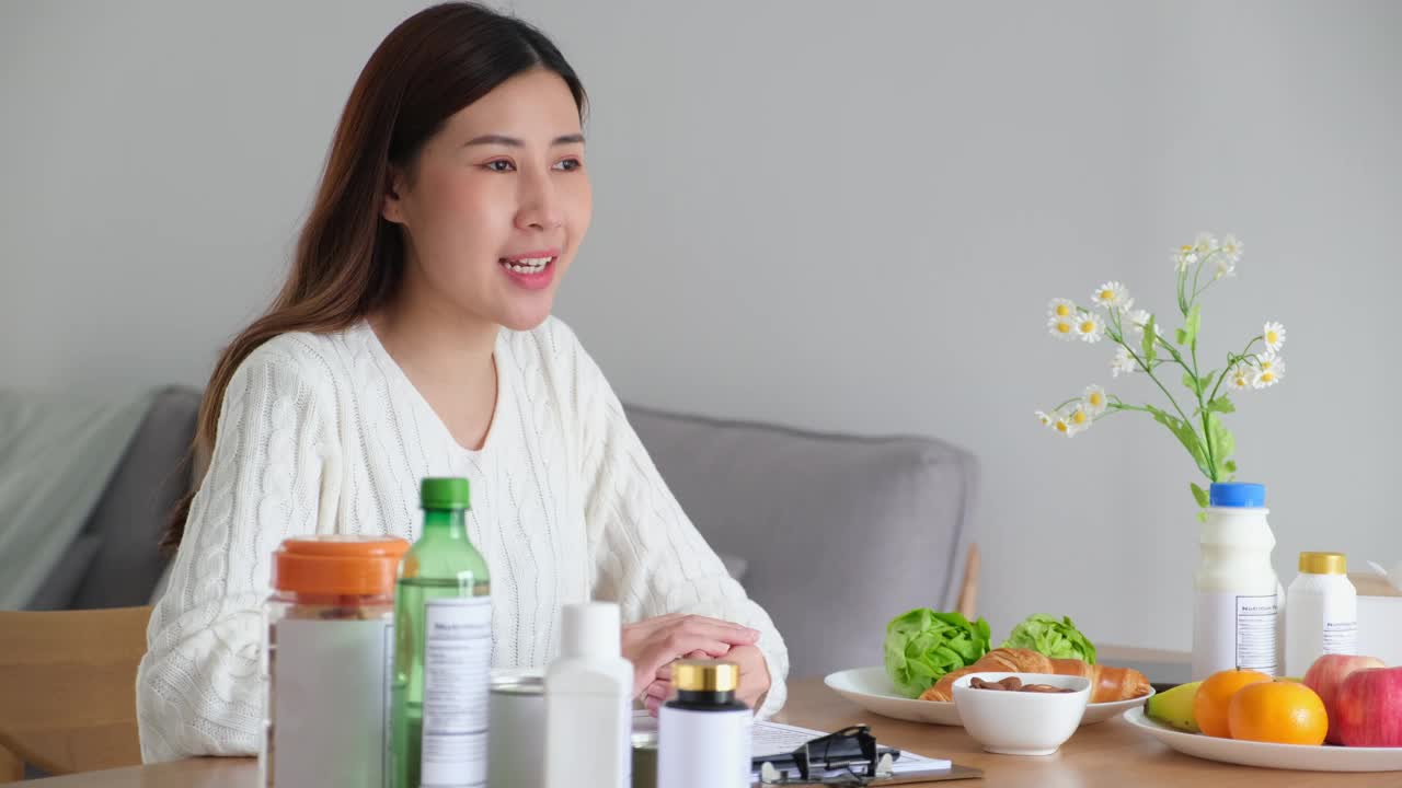 年轻的亚洲女性营养师手持并阅读食品包装上的营养成分标签，为客户提供健康饮食的建议视频下载