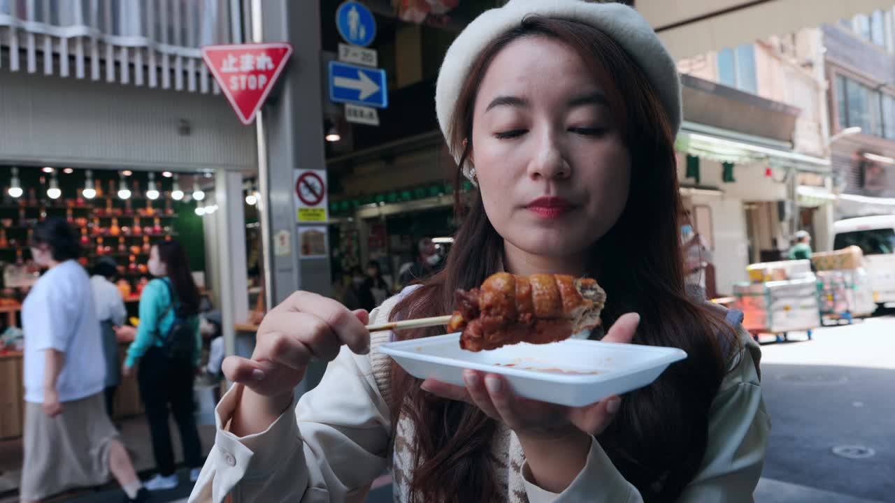 在京都的西木市场，一名亚洲女子正沉浸在日本的美食中，品尝着当地的美食。她沉迷于街头小吃，体验着该地区丰富的风味和文化底蕴。视频下载