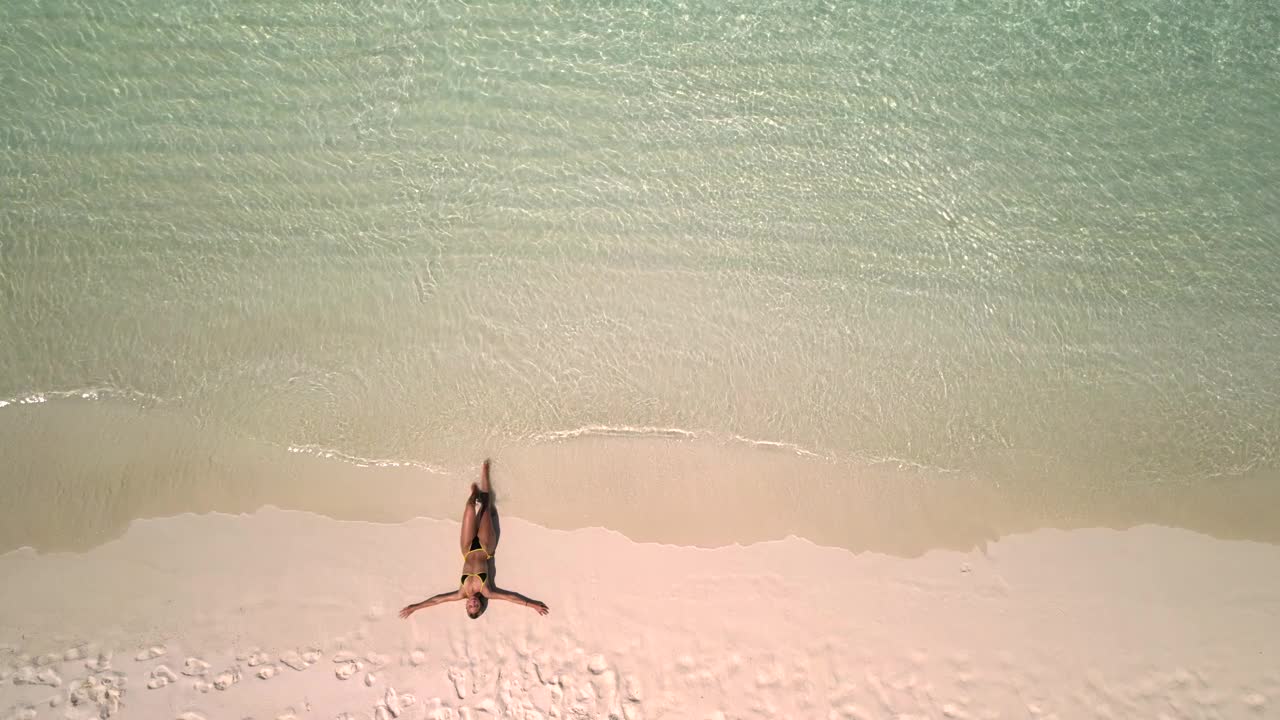 暑假期间，一名年轻女子躺在沙滩上，正在下海。视频下载
