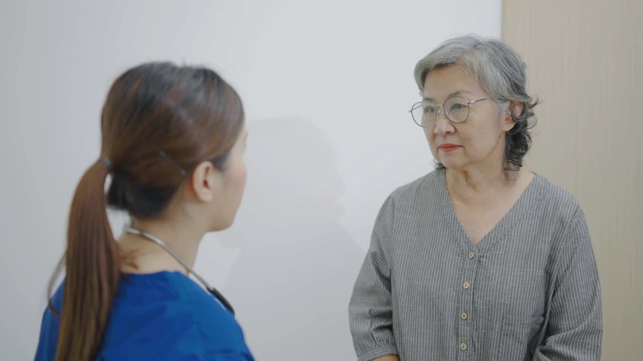 亚洲青年女医生在医院里用听诊器听老年妇女病人的心脏，检查老年妇女的健康，检查成熟中年妇女的肺部。视频下载
