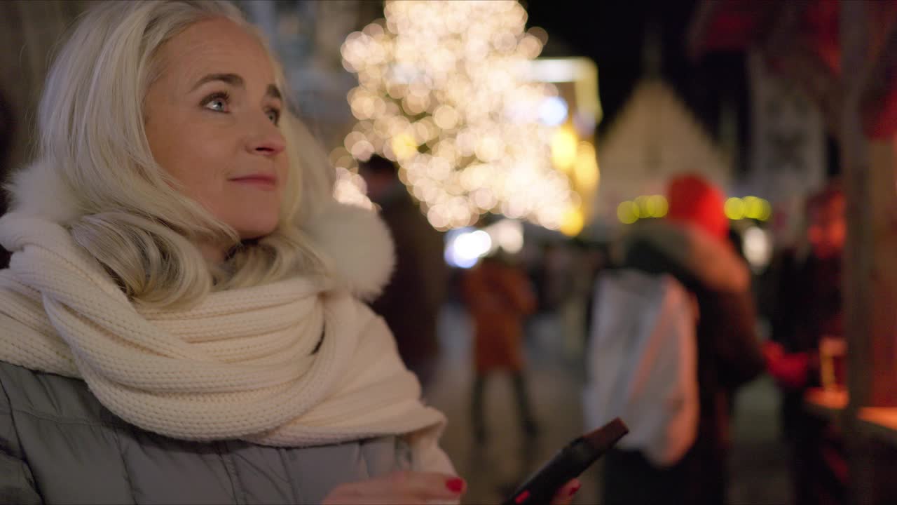 一个成熟的女人在出差期间参观慕尼黑的圣诞市场，在漫长的一天工作后，她享受着一杯热红酒。视频下载