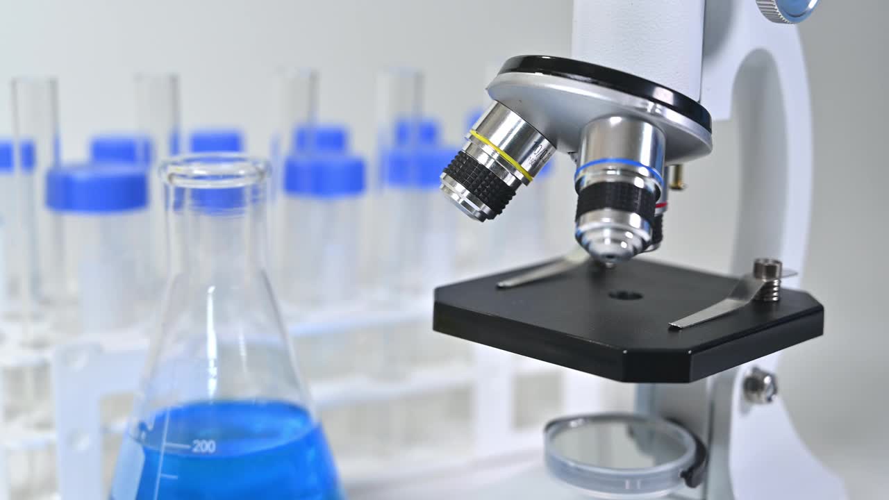 用蓝色液体瓶和显微镜观察科学家的手的特写视频素材
