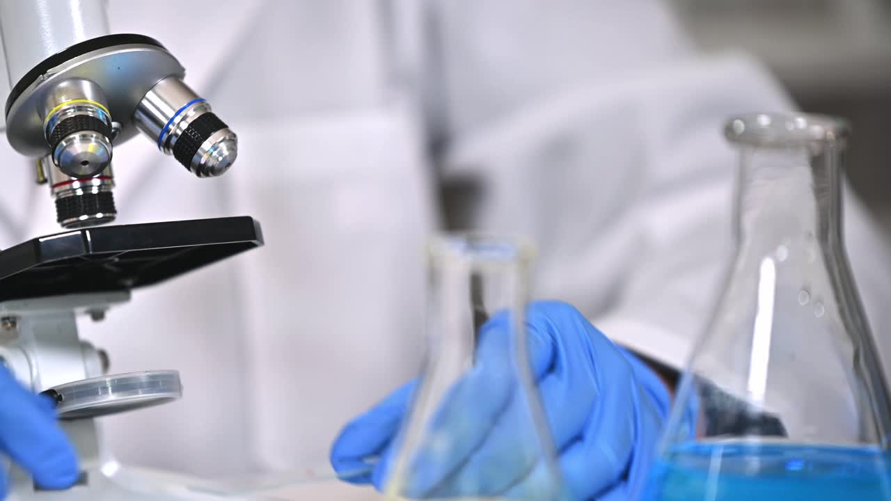 一个戴着蓝色手套，使用显微镜的科学家的手特写视频素材