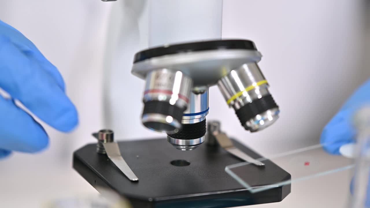 一个戴着蓝色手套，使用显微镜的科学家的手特写视频素材