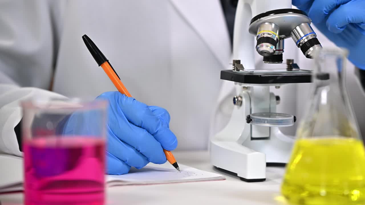 一个戴着蓝色手套，使用显微镜的科学家的手特写视频下载