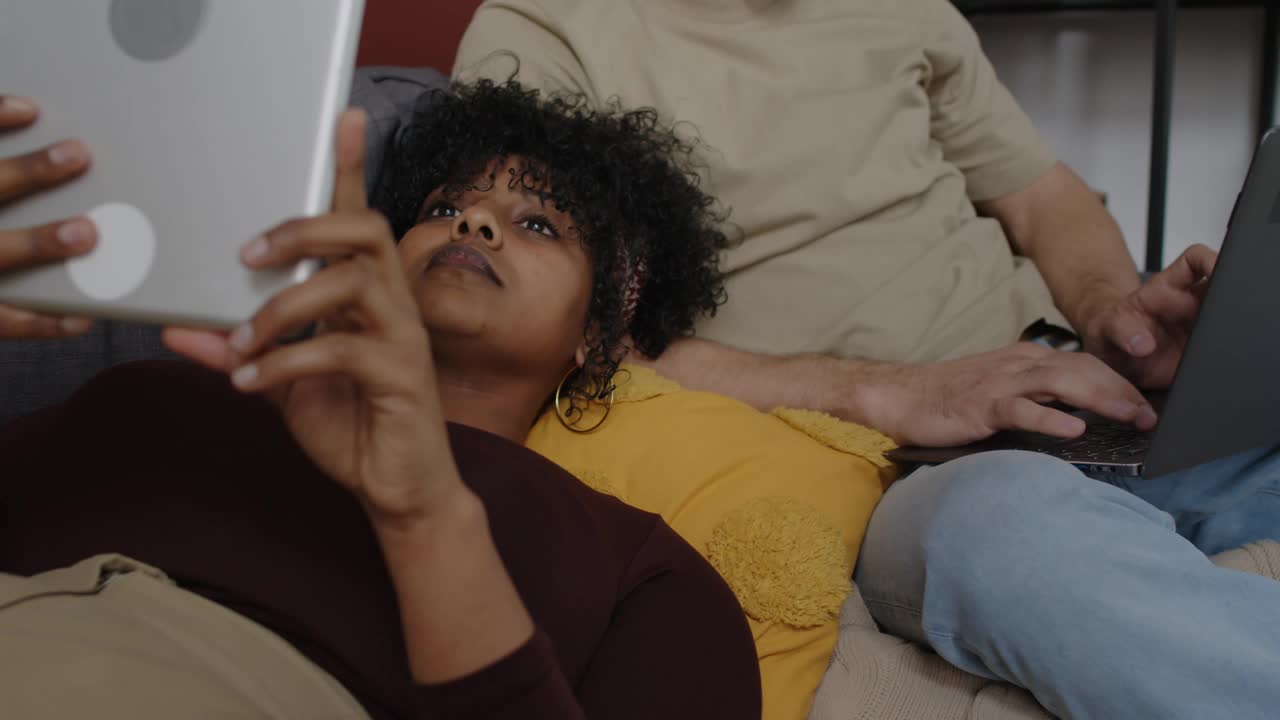 年轻的跨种族夫妇一起在沙发上放松时使用电子产品视频下载