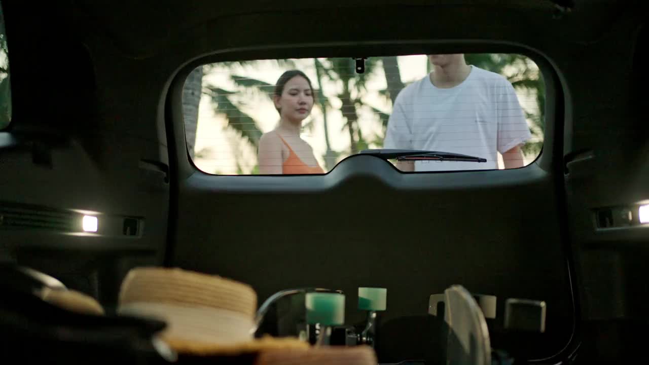 一对快乐的亚洲夫妇从汽车后备箱里拿出一块滑板视频素材