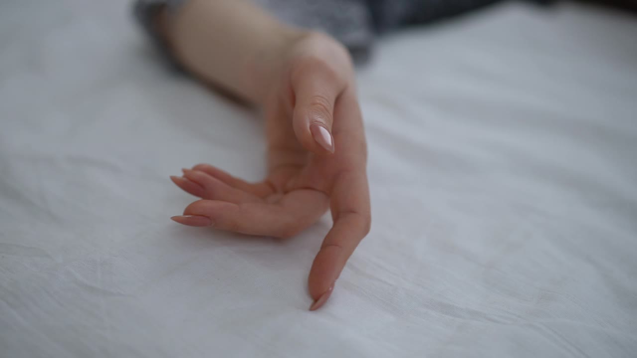 特写镜头。一个女人的手掌躺在一张白色的床单上。修剪整齐的手指慢慢地在床单上来回移动。视频下载