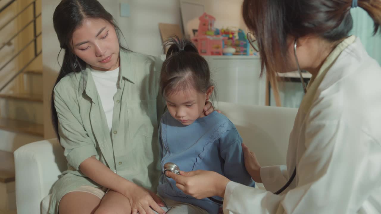 女医生在家里用听诊器检查生病发高烧的女孩。生病女孩因为身体状况和家庭健康和她妈妈住在一起。视频下载
