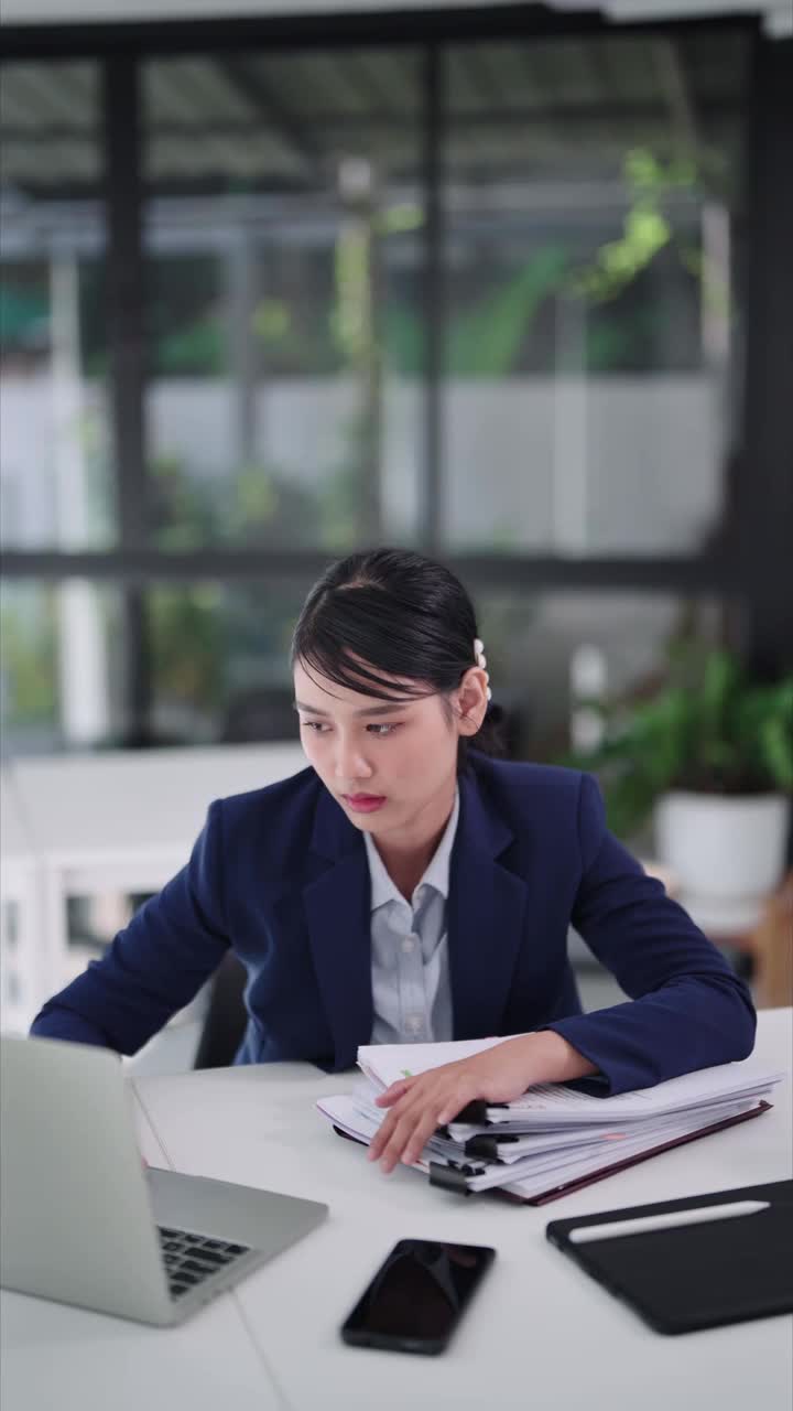 一名亚洲女商人坐在办公桌前对着笔记本电脑工作，感到无聊和困倦，最终进入小睡状态。捕捉办公室远程工作生活的平凡瞬间。视频下载