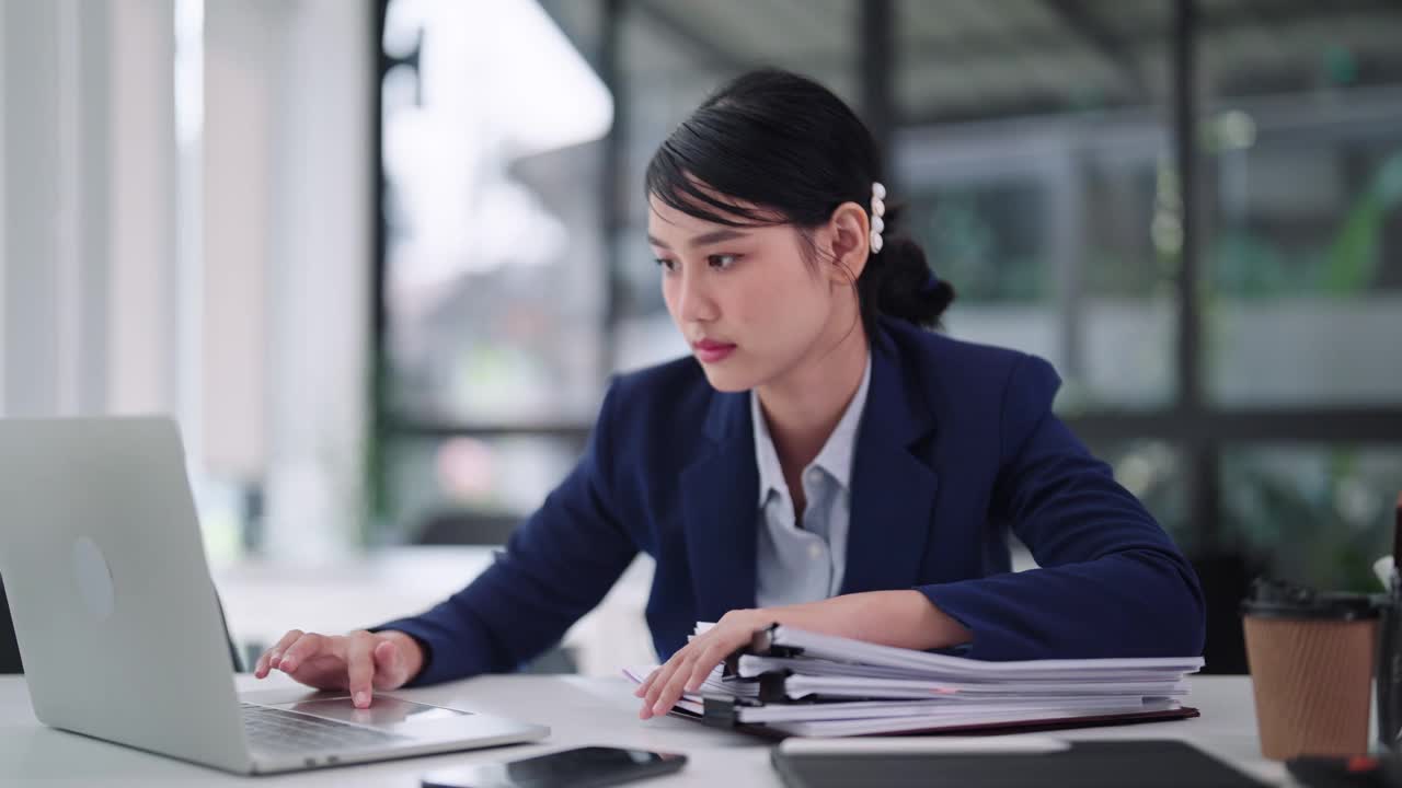 一名亚洲女商人坐在办公桌前对着笔记本电脑工作，感到无聊和困倦，最终进入小睡状态。捕捉办公室远程工作生活的平凡瞬间。视频下载