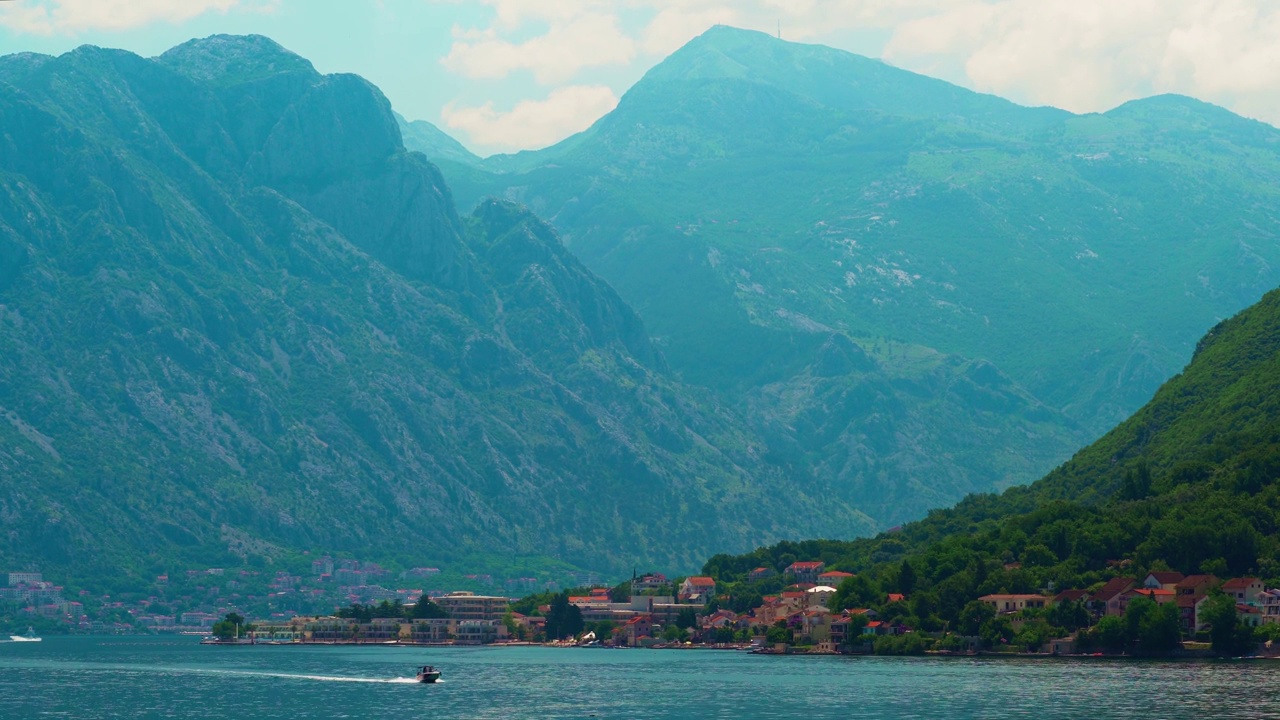 一艘摩托艇沿着海湾航行，背景是山脉和岸边的小镇，阳光明媚的日子里美丽的海景，夏日旅行的概念视频下载