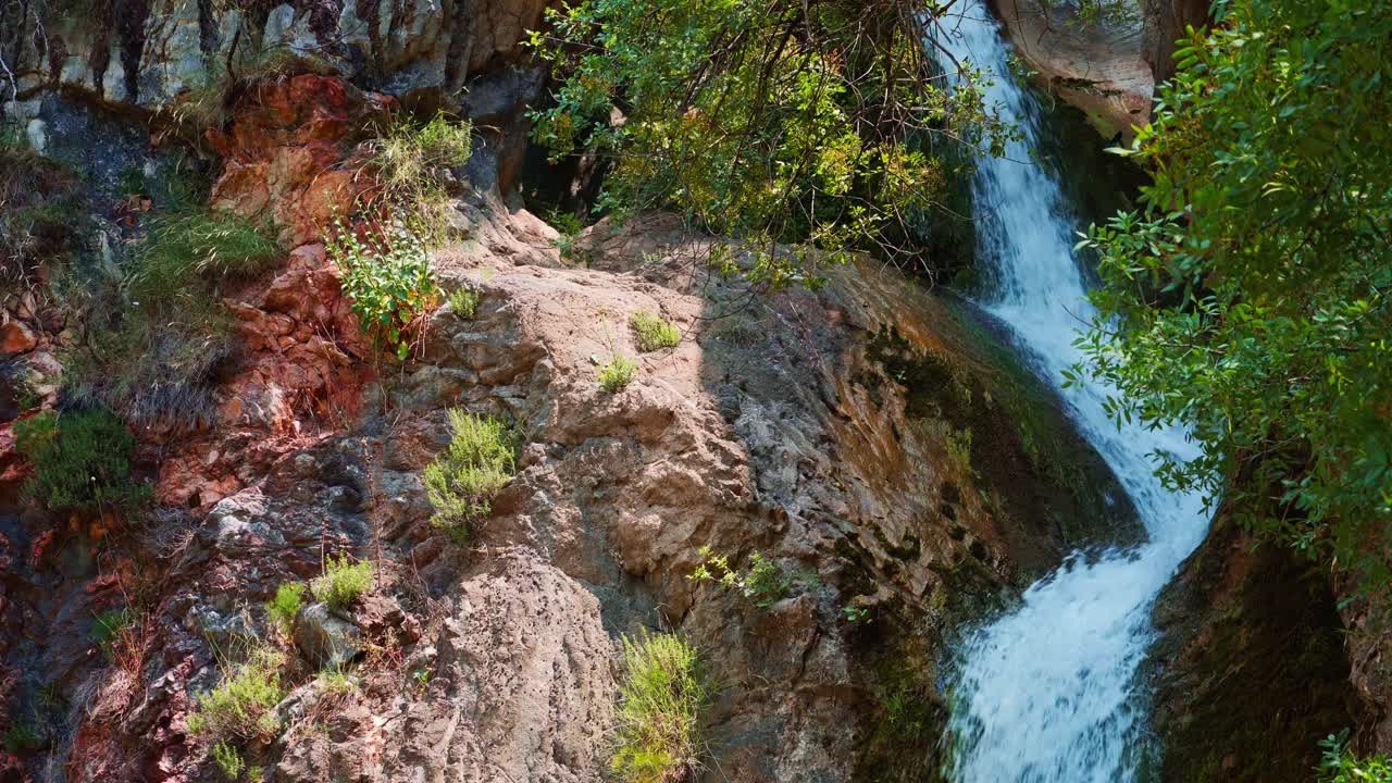 一个瀑布和一个小湖在山上，水倾泻在岩石的背景，一个美丽的夏日景观在一个明媚的阳光灿烂的日子视频下载
