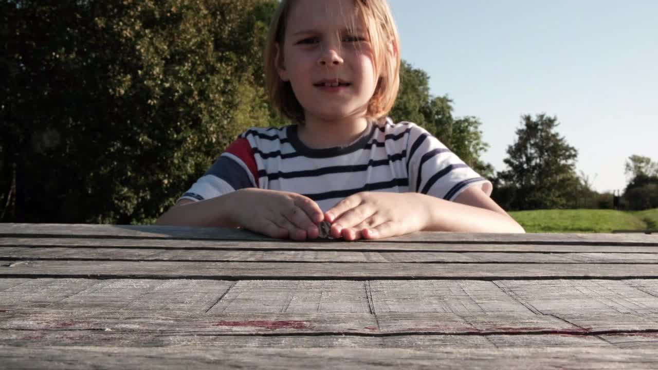 户外的乐趣:一个年轻的长发男孩在木桌上玩玻璃弹珠游戏视频下载