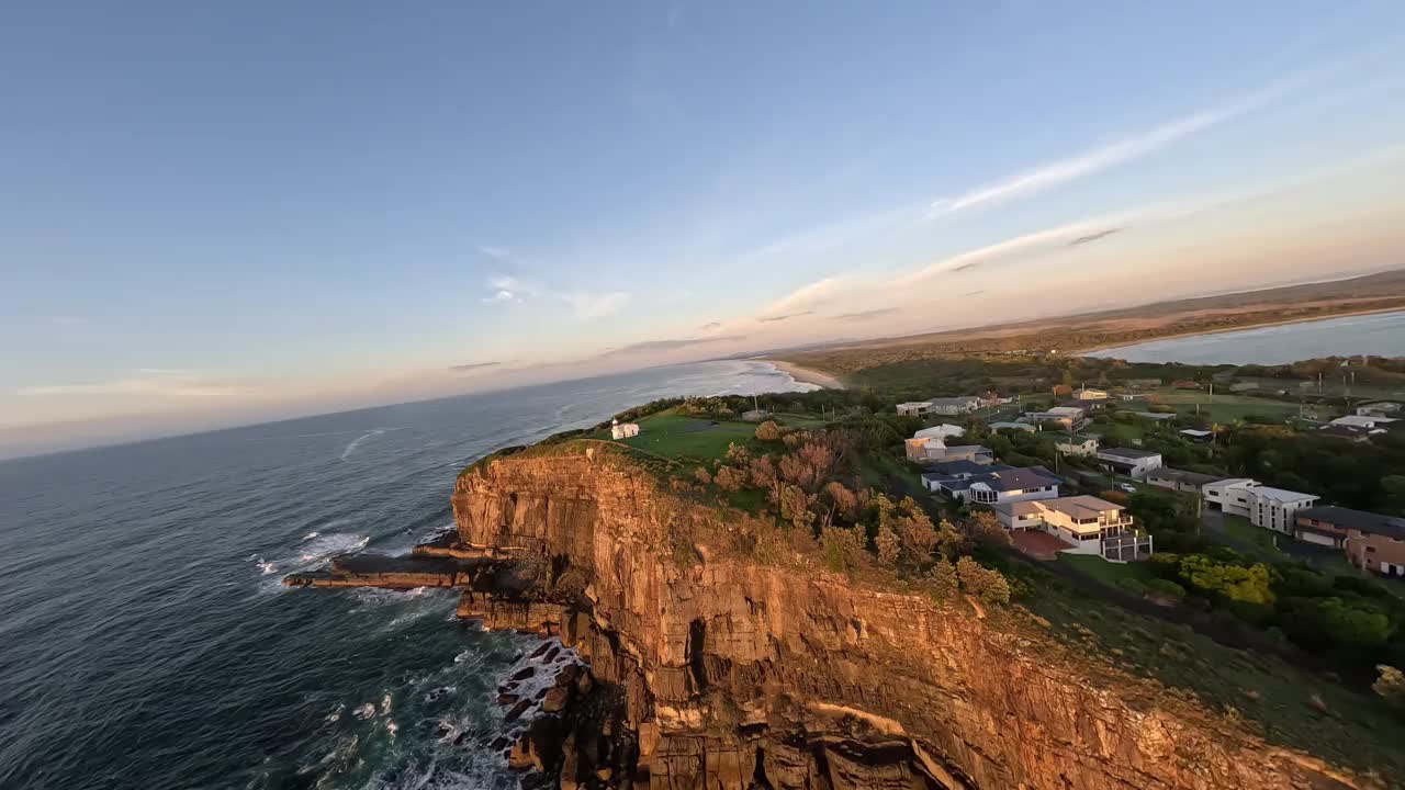 从悬崖边飞过的鸟瞰图，经过眺望日出和灯塔的成年人。视频下载
