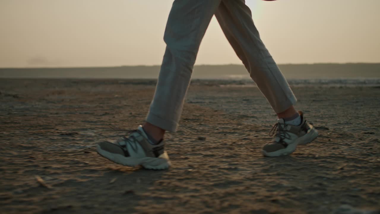 一个夏天的晚上，一个女孩在城外度假，穿着灰色短裤和运动鞋，走在荒芜的海边视频下载